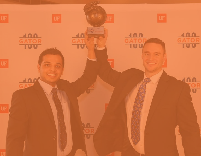 Karthik and partner, Luke, pose holding a trophy in recognition at the Gator 100 ceremony.