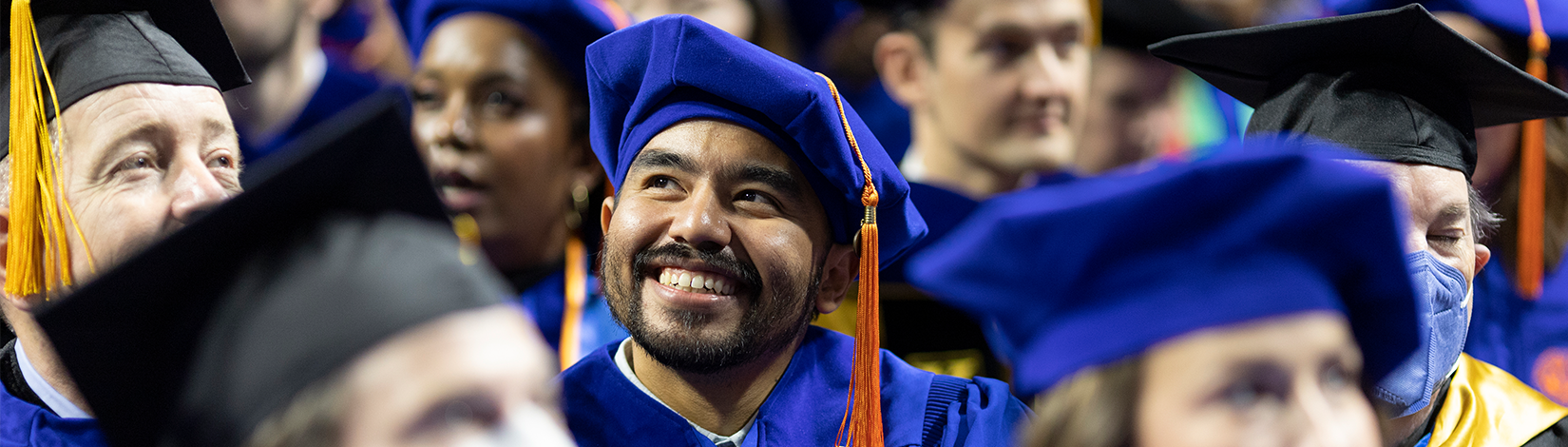 Graduating masters degree student in full graduation regalia glances upward during commencement.