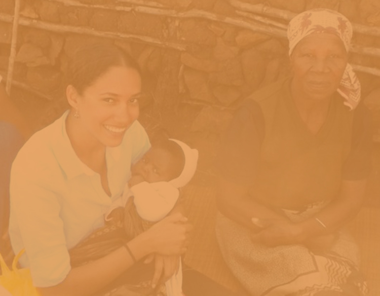 female CALS student studying abroad in Swaziland holding a child and sitting next to a local resident. 