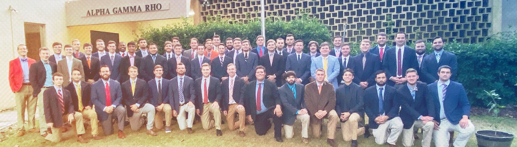 30 young men in professional clothing pose for a photo outside the Alpha Gamma Rho house. 