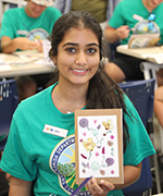 A young woman in a green shirt, holding a hand painted card of flowers.