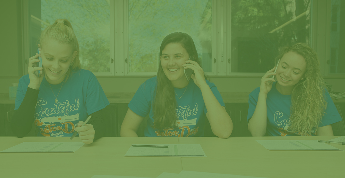 Three female CALS students sitting at a table calling potential donors for the student philanthropy council on their cell phones. 