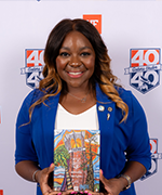 A woman in a blue blazer and white shirt stands holding a piece of artwork after receiving an award.