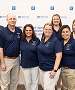 A group of three women and one man in navy blue polos crowd together for a photo.