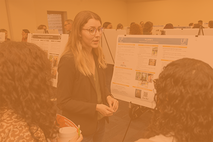 Student speaks to peers while standing in front of her research poster.