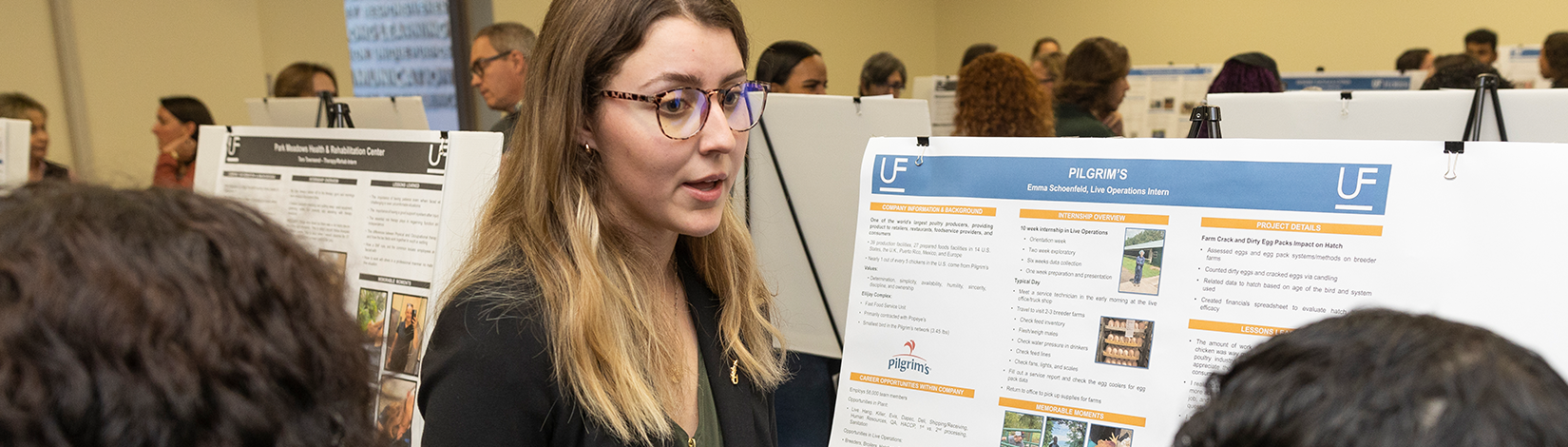 Student speaks to peers while standing in front of her research poster.