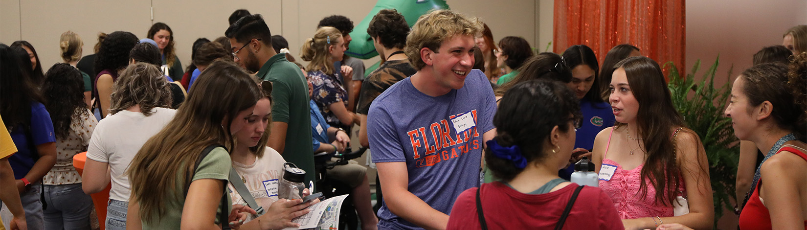 Students standing around round tables talking at an event.