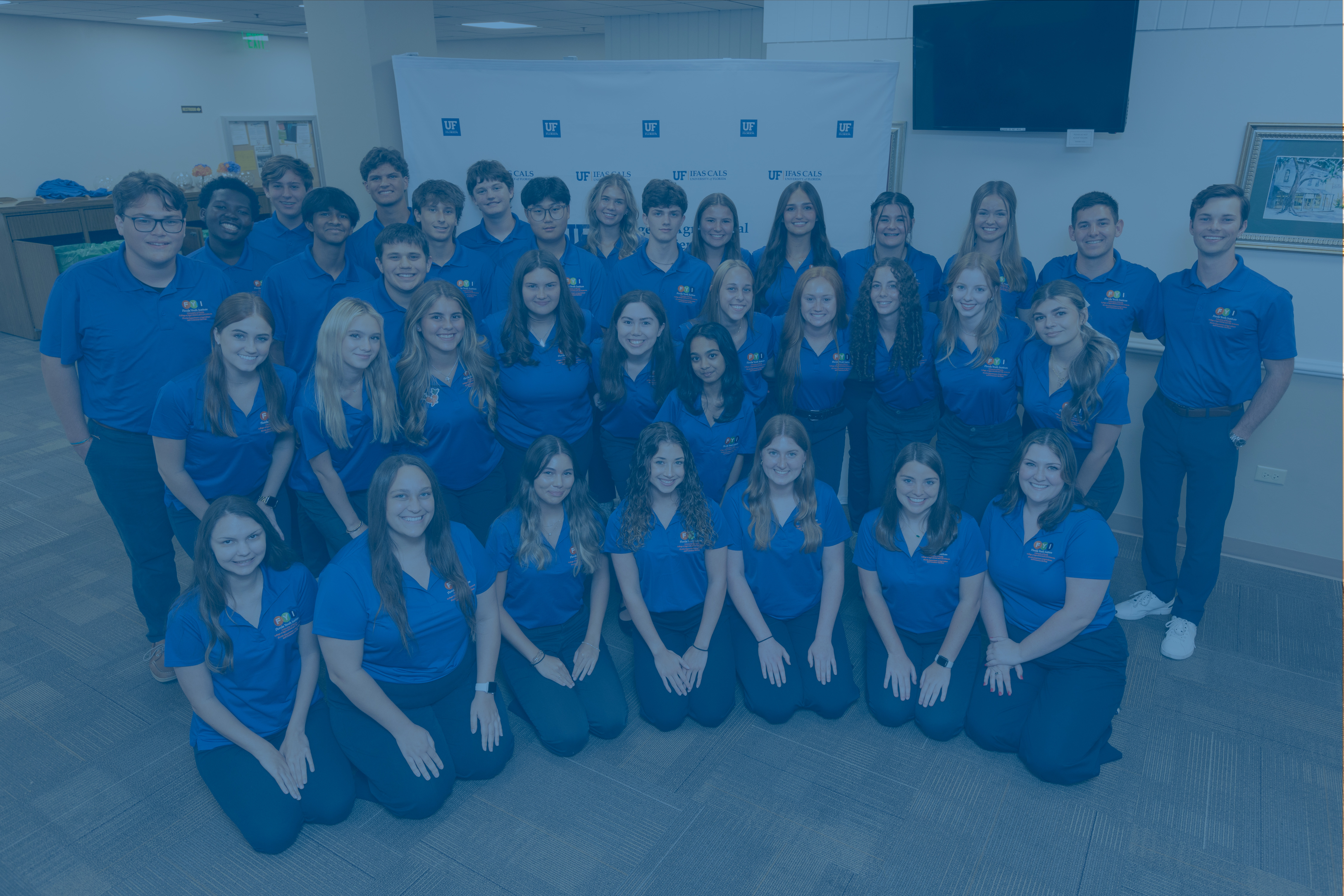 Students in blue shirts standing and kneeling for a group picture.