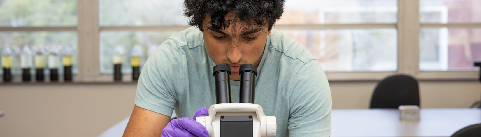 Student looks through microscope while adjusting knob.