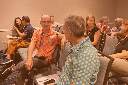 A diverse group of individuals seated in chairs, engaged in discussion within a modern conference room setting.