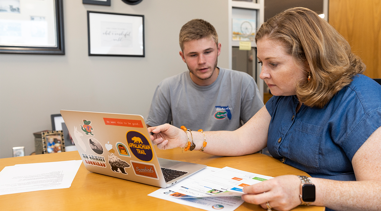 A college student and staff member sit in front of a laptop. The staff member points at the laptop.